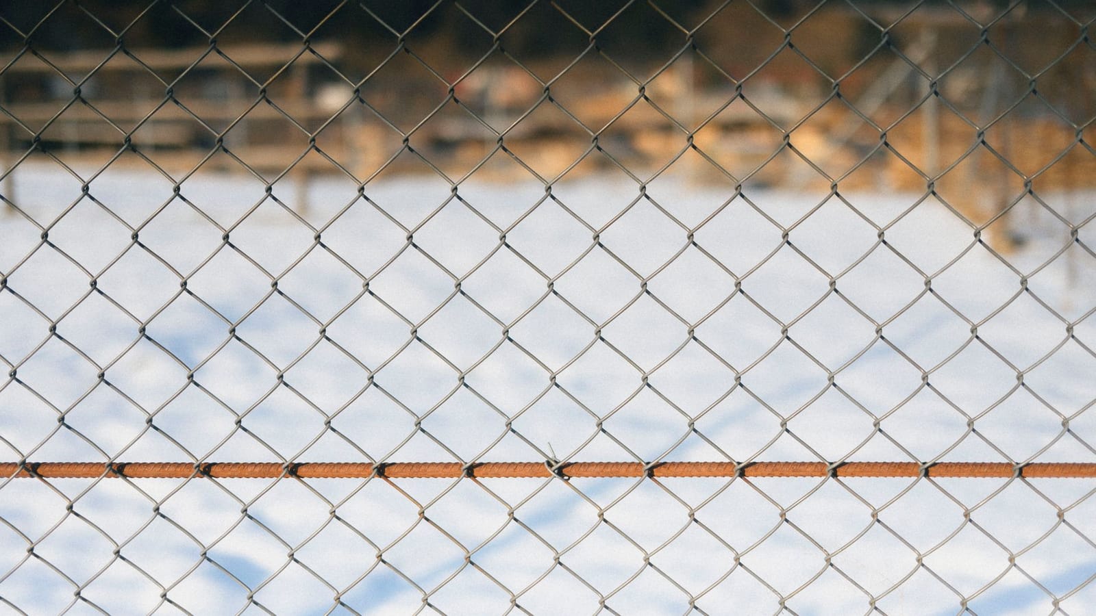 A chain link fence in sharp focus with a soft snowy backdrop, capturing a serene winter scene.