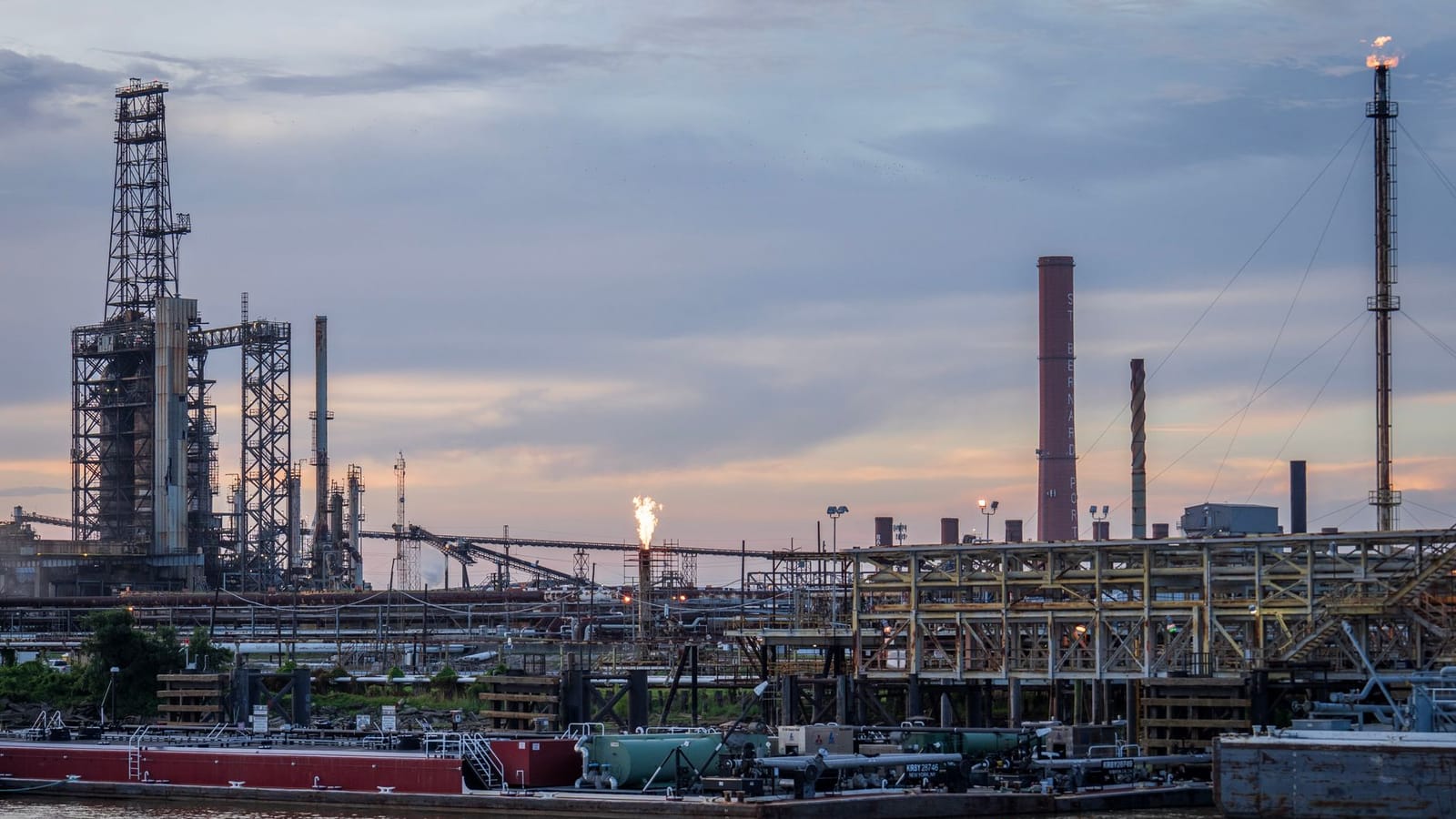 A large industrial refinery complex next to a river with a sunset backdrop.