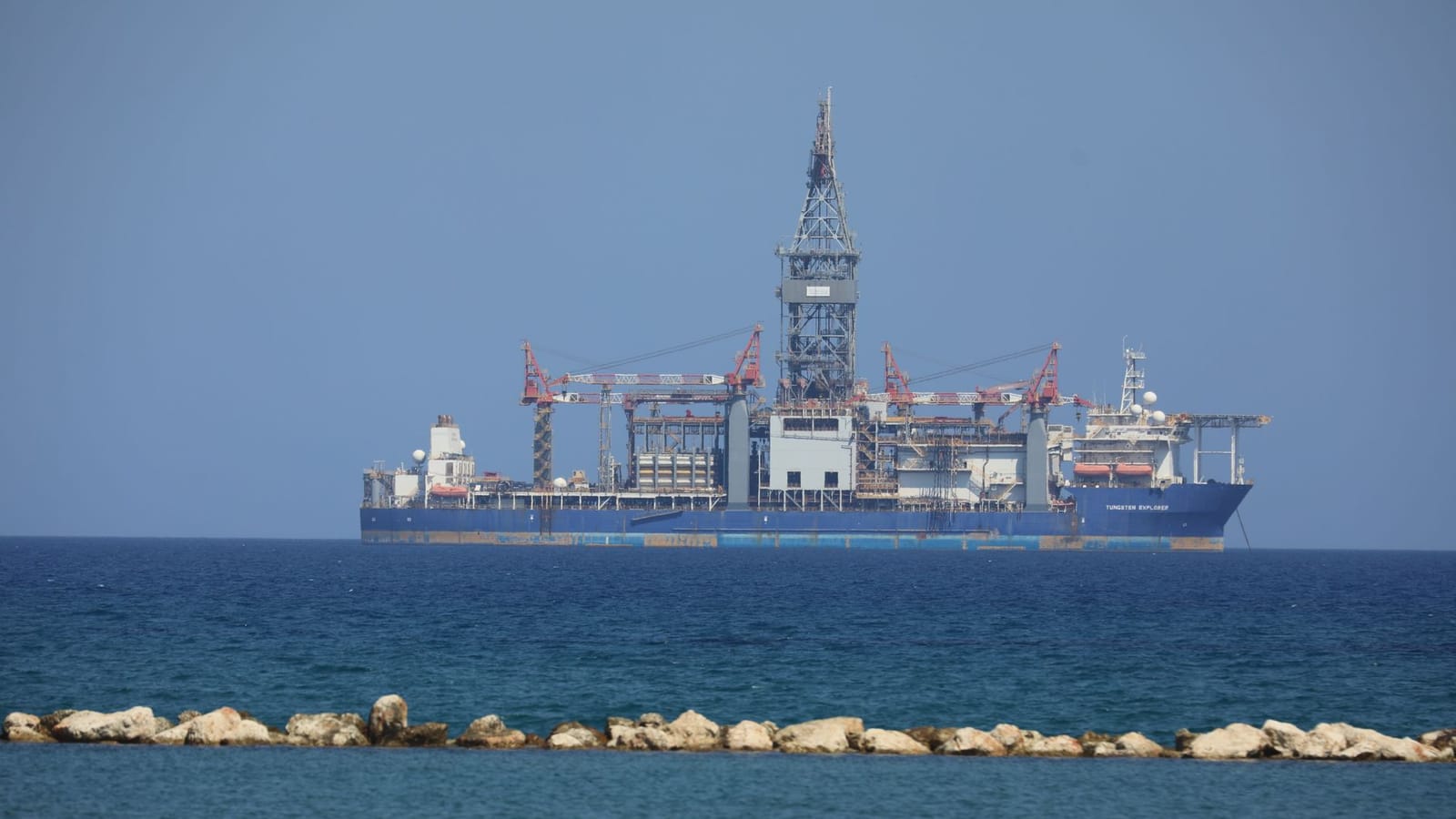 An offshore drilling rig floats on a calm sea with a clear blue sky in the background.