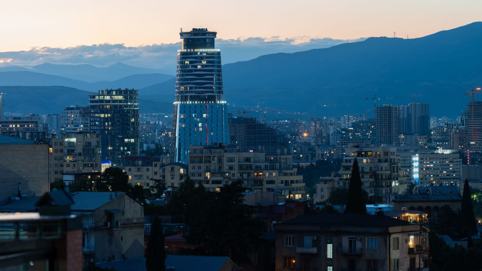 Twilight view of Tbilisi's skyline highlighting a distinctive modern skyscraper against mountain backdrop.
