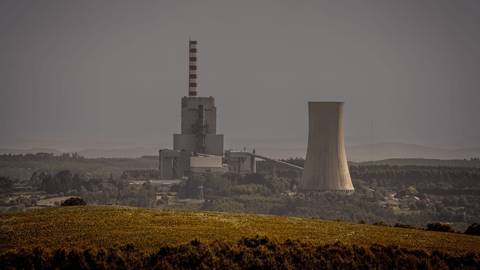 Distant view of a power plant with cooling towers amidst a vast landscape, illustrating energy production.