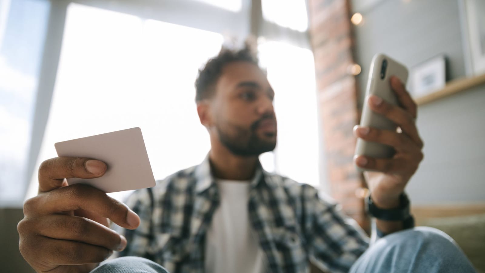 A man using a smartphone and card for online shopping in a cozy indoor setting.