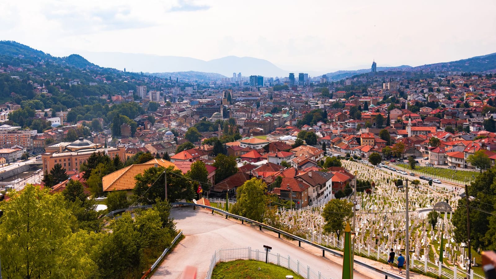 Aerial view of Sarajevo, showcasing cityscape, red rooftops, and distant mountains.