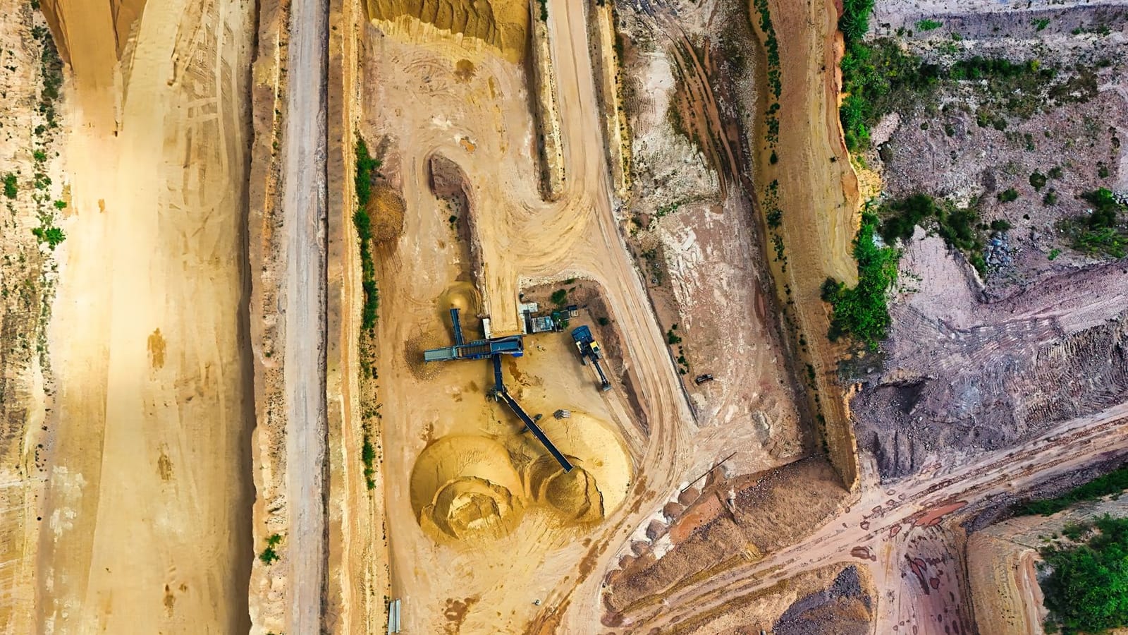An aerial shot of an open-pit mine with machinery and pathways visible, surrounded by landscape.