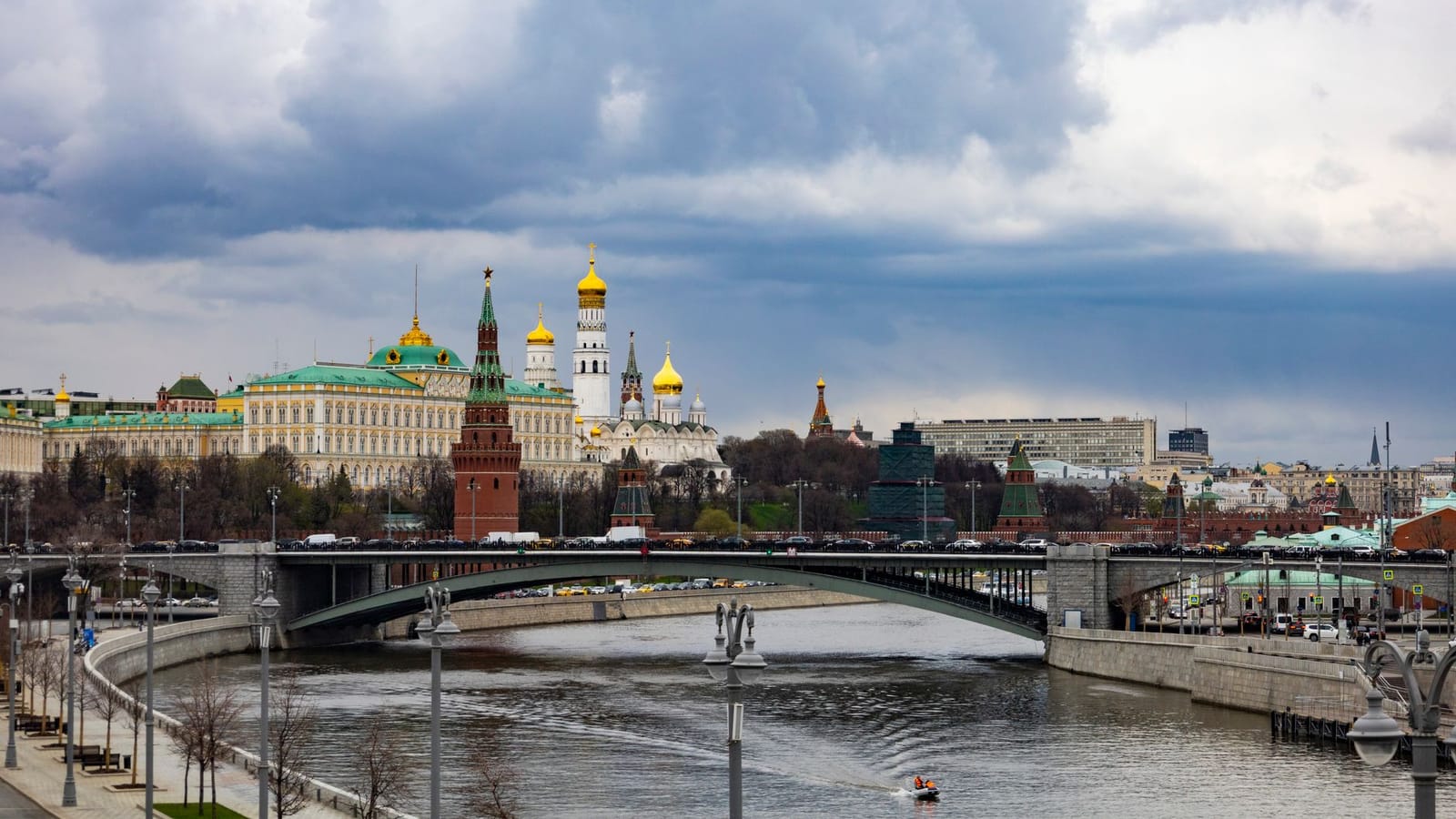 A picturesque view of the Moscow Kremlin with a bridge over the Moskva River under a dramatic sky.