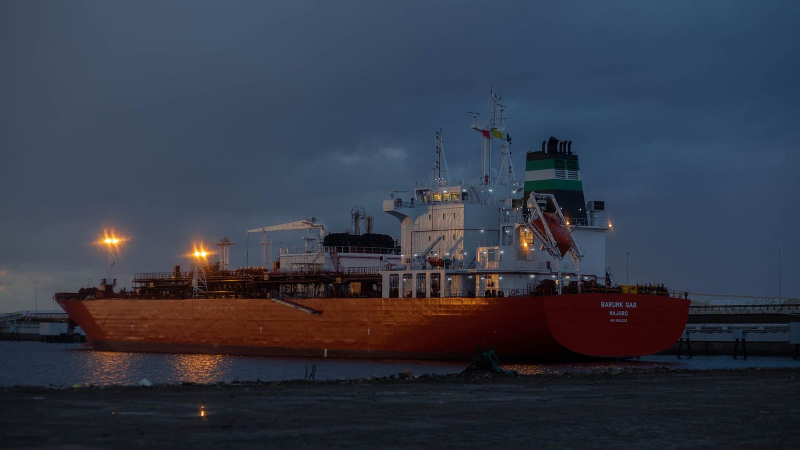 A large oil tanker ship illuminated at night, docked at a harbor.
