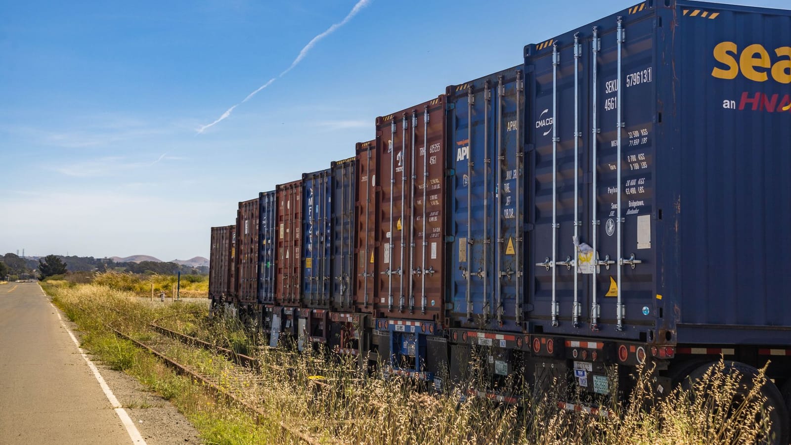 Colorful cargo containers on a freight train along a rural railway track under a clear blue sky.