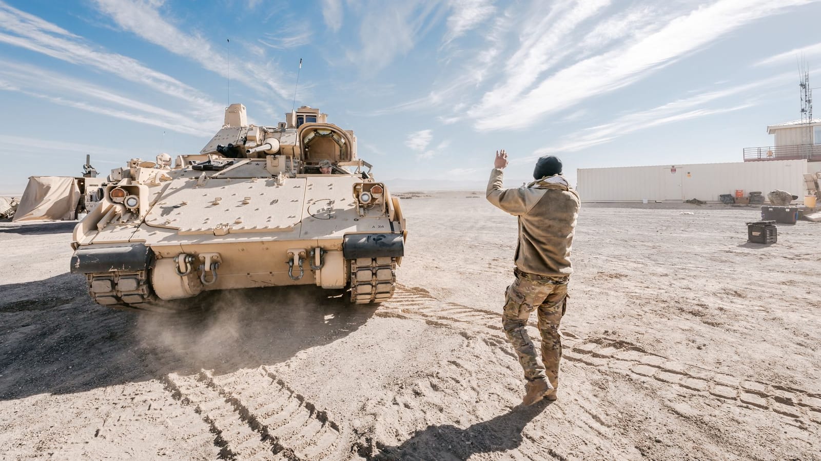 Bradley Fighting Vehicle and soldier in desert training operation under clear sky.